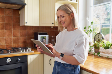 Mid adult woman using digital tablet while standing in a kitchen at home - Powered by Adobe