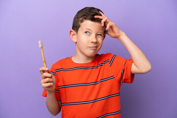Little boy brushing teeth isolated on purple background having doubts and with confuse face...