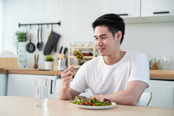 Asian attractive handsome male eating green salad in kitchen at home. 