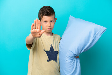 Little boy in pajamas isolated on blue background making stop gesture