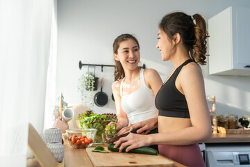 Asian young two women sibling in sportswear cooking salad in kitchen.