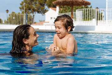 Fototapeta na wymiar Mother and son bathing in the pool,both of them smiling happily looking at each other while enjoying