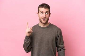 Young caucasian man isolated on pink background thinking an idea pointing the finger up