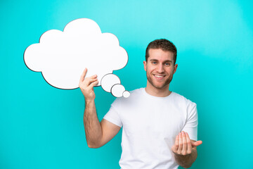 Young caucasian man isolated on blue background holding a thinking speech bubble and doing coming gesture