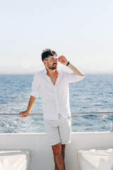 A young smiling happy man on the deck of a cruise ship looks towards the sunset of a blue sky.