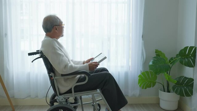 Asian senior male sit alone on wheelchair and looks family photographs	