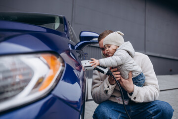 father playing with daughter while charging electric car - obrazy, fototapety, plakaty