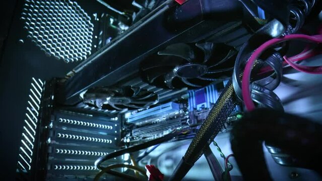 View from inside of old computer system unit. Camera movement zooms in on coolers, that run and then stop. Close up background of computer structure with wires, processor and fans with dust particles.