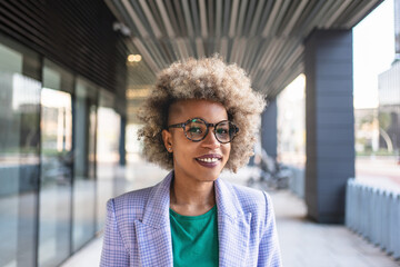 Smiling African American business woman with afro hair standing in hallway outside building during...