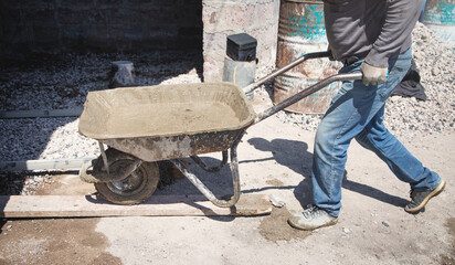 Construction worker pushing wheelbarrow of cement.