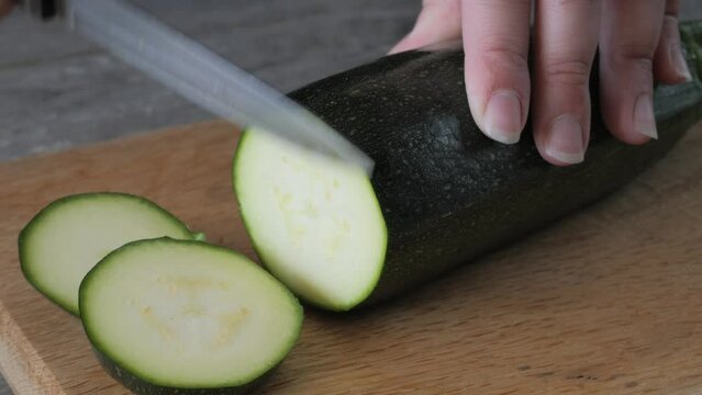 Female hands cutting zucchini on a wooden board, close up. Cooking a fresh vegetables