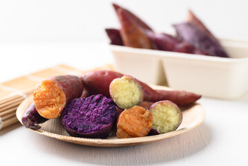 Purple, orange and yellow sweet potatoes in natural plate on white background