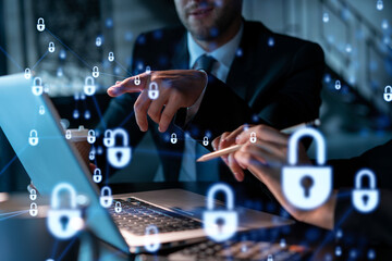 Two colleagues working together to protect clients confidential information and cyber security. IT hologram padlock icons modern office background at night time