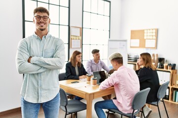 Young hispanic businessman smiling happy standing with arms crossed gesture at the office during business meeting.