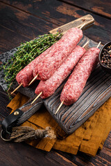 Fresh Raw kofta or lula kebabs skewers on wooden board with thyme. Wooden background. Top view