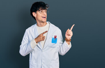 Handsome hipster young man wearing doctor uniform smiling and looking at the camera pointing with two hands and fingers to the side.