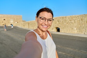 Woman taking photo against the backdrop of historic fortress, sea bay