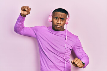 Young black man dancing listening to music using headphones skeptic and nervous, frowning upset...