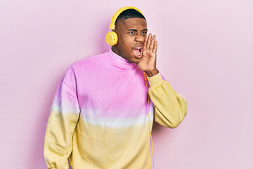 Young black man listening to music wearing headphones shouting and screaming loud to side with hand on mouth. communication concept.