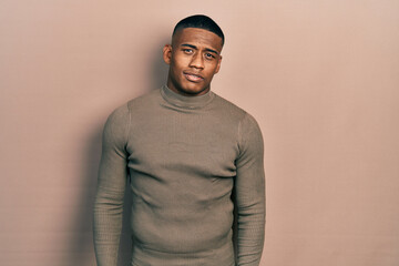 Young black man wearing casual turtleneck sweater relaxed with serious expression on face. simple and natural looking at the camera.