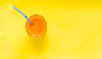 A Glass of Cool pumpkin juice with straw on pastel yellow background.