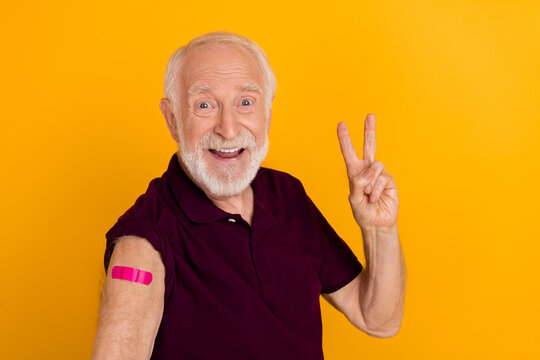 Photo of cheerful aged man show fingers cool v-symbol vaccinated covid protection isolated over yellow color background