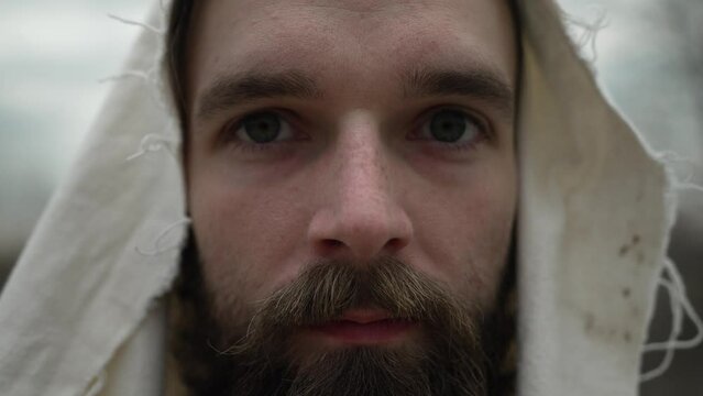 Closeup of the eyes of Jesus Christ or spiritual, religious old or new testament bible man with beard looking up at the camera with a slight smile on his face in slow motion.