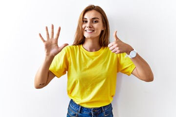 Young brunette woman standing over isolated background showing and pointing up with fingers number six while smiling confident and happy.