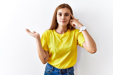 Young brunette woman standing over isolated background confused and annoyed with open palm showing copy space and pointing finger to forehead. think about it.