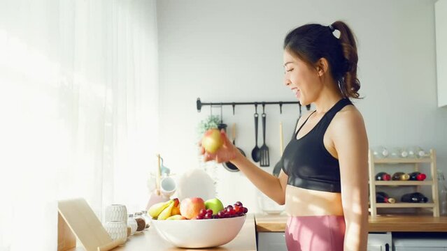 Asian attractive woman eat an apple on dinner table in kitchen at home