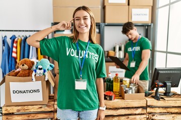 Young blonde girl wearing volunteer t shirt at donation stand smiling pointing to head with one...