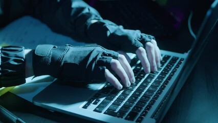 Closeup shot of human hands in fingerless gloves typing on grey keyboard in dark room while hacking or coding at night. Low key. IT, modern technology, work, hacking concept