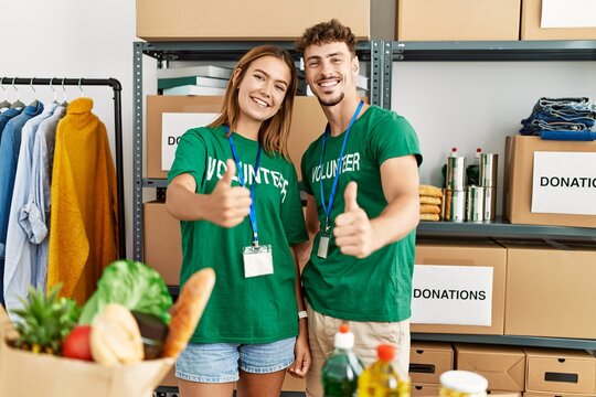 Young hispanic volunteer couple smiling happy doing ok sign with thumbs up at charity center.