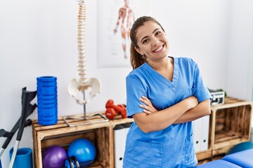 Young hispanic woman wearing physiotherapy uniform standing with arms crossed gesture at sport...