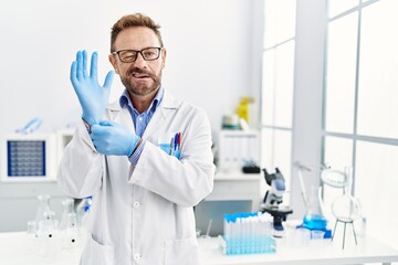Middle age man working at scientist laboratory winking looking at the camera with sexy expression,...