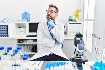 Fototapeta premium Middle age man working at scientist laboratory serious face thinking about question with hand on chin, thoughtful about confusing idea