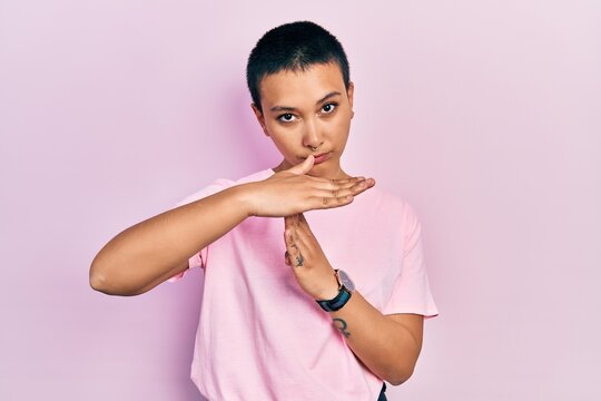 Beautiful hispanic woman with short hair wearing casual pink t shirt doing time out gesture with hands, frustrated and serious face