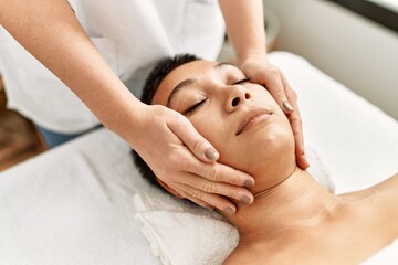 Young hispanic woman having facial massage at beauty center