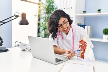 Young latin woman wearing doctor uniform holding anatomical model of respiratory system at clinic