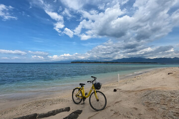 Fototapeta premium Yellow bicycle parking at the sandy beach under dramatic blue sky, sea side. 