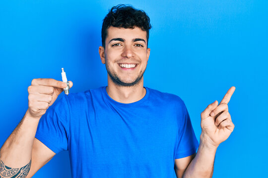 Young hispanic man holding spark plug smiling happy pointing with hand and finger to the side