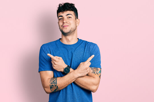 Young hispanic man wearing casual t shirt pointing to both sides with fingers, different direction disagree