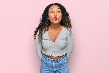 Young hispanic woman with curly hair wearing casual clothes making fish face with lips, crazy and...