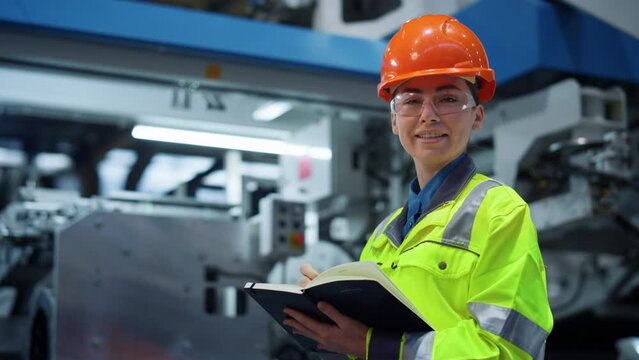 Woman factory worker looking camera near big metal manufacture constructions. 