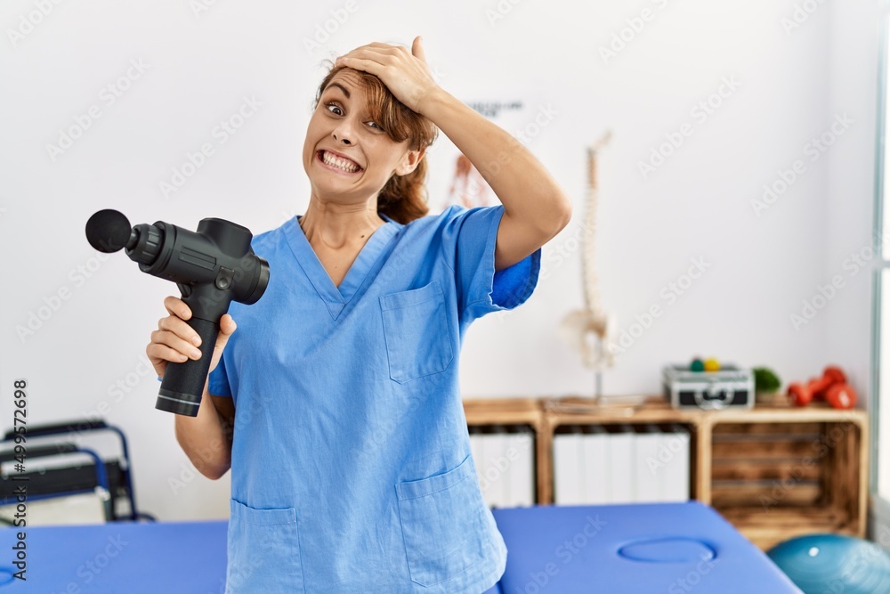 Sticker Beautiful caucasian woman holding therapy massage gun at wellness center stressed and frustrated with hand on head, surprised and angry face