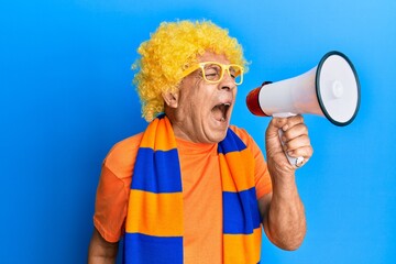 Senior hispanic hooligan man wearing crazy look with glasses and wig supporting football team...