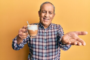 Handsome senior man with grey hair drinking a cup coffee smiling cheerful offering palm hand giving assistance and acceptance.