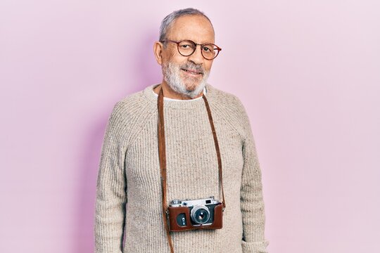 Handsome senior man with beard holding vintage camera with a happy and cool smile on face. lucky person.