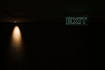 Green exit sign isolated in dark black room with little yellow  spotlight