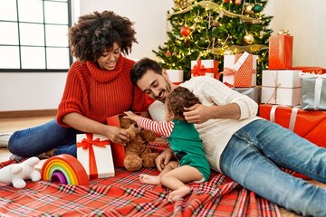 Couple and daughter playing with toys sitting by christmas tree at home